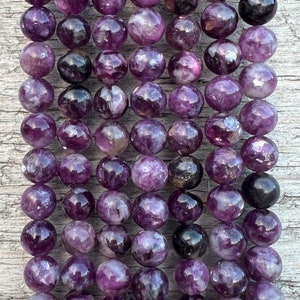 May include: A strand of purple amethyst beads, each bead is round and has a unique pattern of swirls and inclusions. The beads are arranged in rows, creating a visual texture.