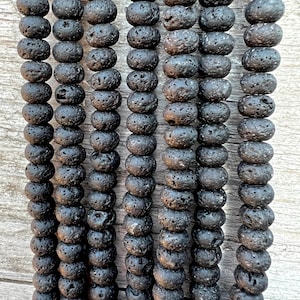 Peut inclure: Gros plan sur un brin de perles en roche volcanique noire. Les perles sont rondes et ont une surface rugueuse et texturée.