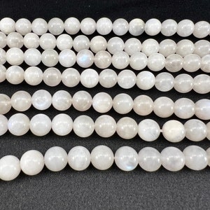 Può includere: Fili di perline di pietra di luna bianca. Ogni perla è rotonda e ha una lucentezza perlacea e iridescente. Le perle sono infilate insieme, creando una linea continua di sfere luminose. Le perle hanno un diametro di circa 8 mm.