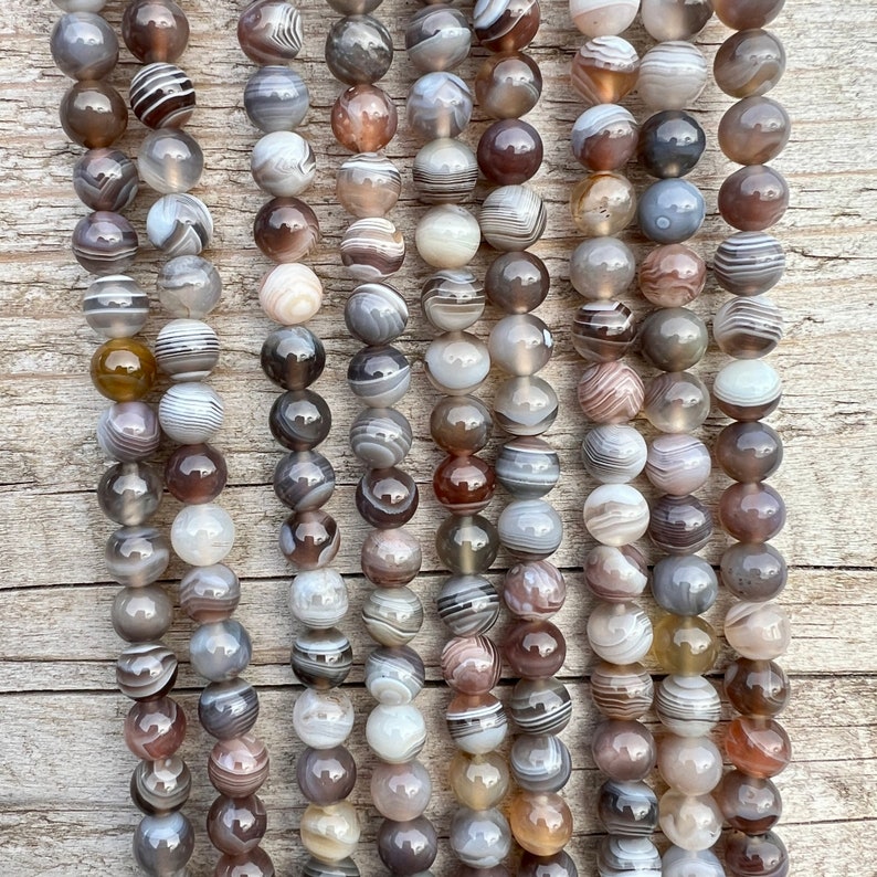 Botswana Agate beads strands lain on a bright wood board in outdoors under natural daylight.