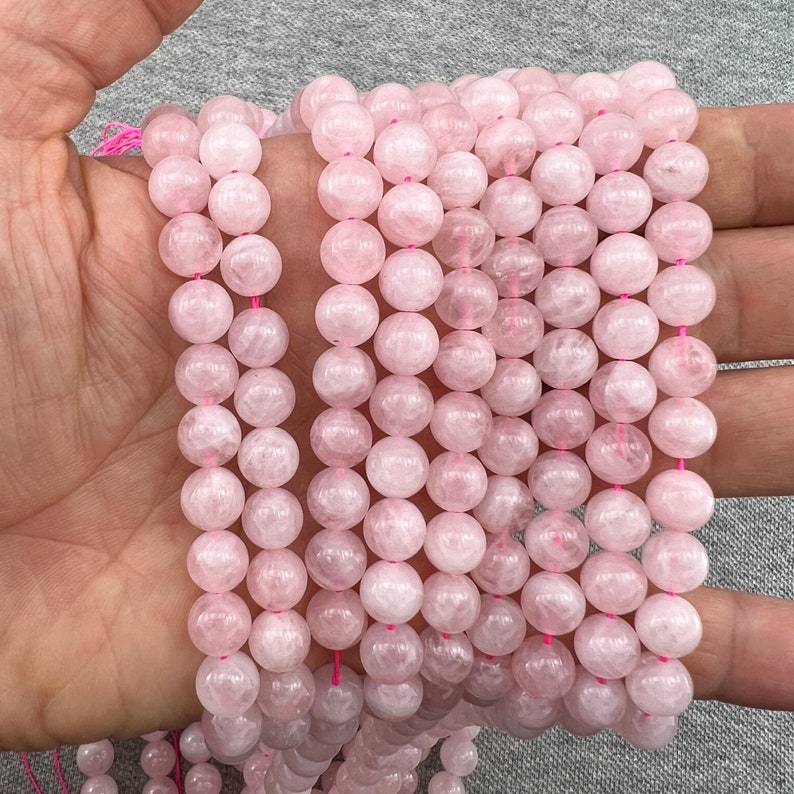 8mm Madagascar rose quartz beads strands held in hand on a grey background