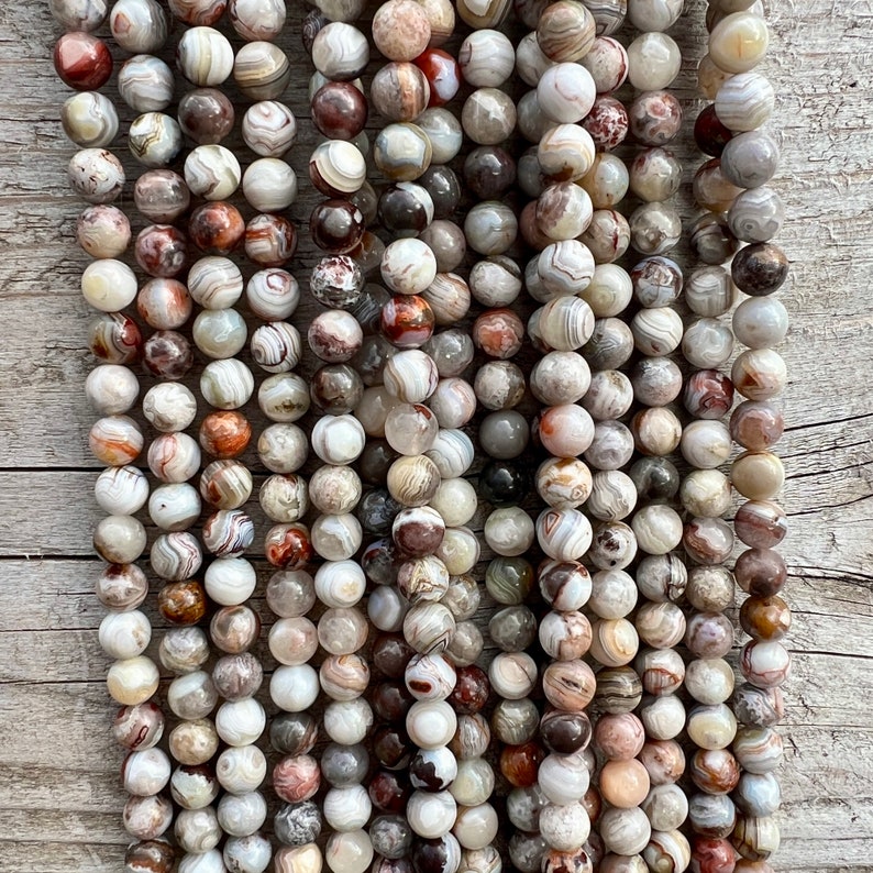 Laguna Lace Agate beads strands laid on a bright wood board in outdoors under natural daylight. these beads are white and gray and have lots of veins in various shapes and colors from red to brawn or pale blue