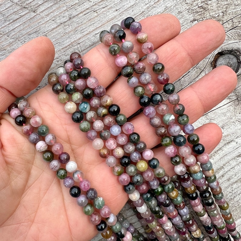 Tourmaline stone 6mm beads strands held in hand over a bright wood board at outdoors and pictured under natural day light