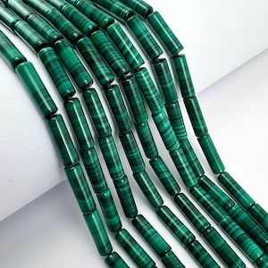 Könnte beinhalten: Nahaufnahme von Strängen zylindrischer Malachitperlen. Die Perlen sind tiefgrün mit dunkleren grünen Bändern, wodurch ein Streifenmuster entsteht. Die Perlen sind aufgefädelt und eignen sich für die Schmuckherstellung.