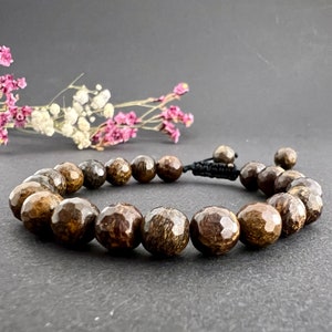 Op de afbeelding: Een bruine houten kralen armband met een zwarte koordsluiting. De kralen zijn gefacetteerd en hebben een natuurlijk houtnerfpatroon.