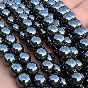 Op de afbeelding: Een streng glanzende zwarte hematiet kralen. De kralen zijn rond en glad en hebben een metallic glans.