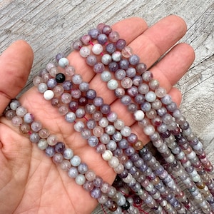 Cherry Tourmaline gemstone 6mm beads strands held in hand on a bright wood board in outdoors under natural daylight.
