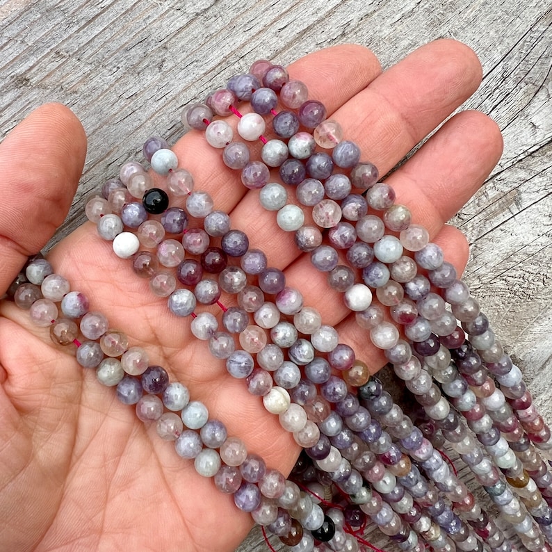 Cherry Tourmaline gemstone 6mm beads strands held in hand on a bright wood board in outdoors under natural daylight.