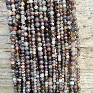 Botswana Agate beads strands lain on a bright wood board in outdoors under natural daylight.