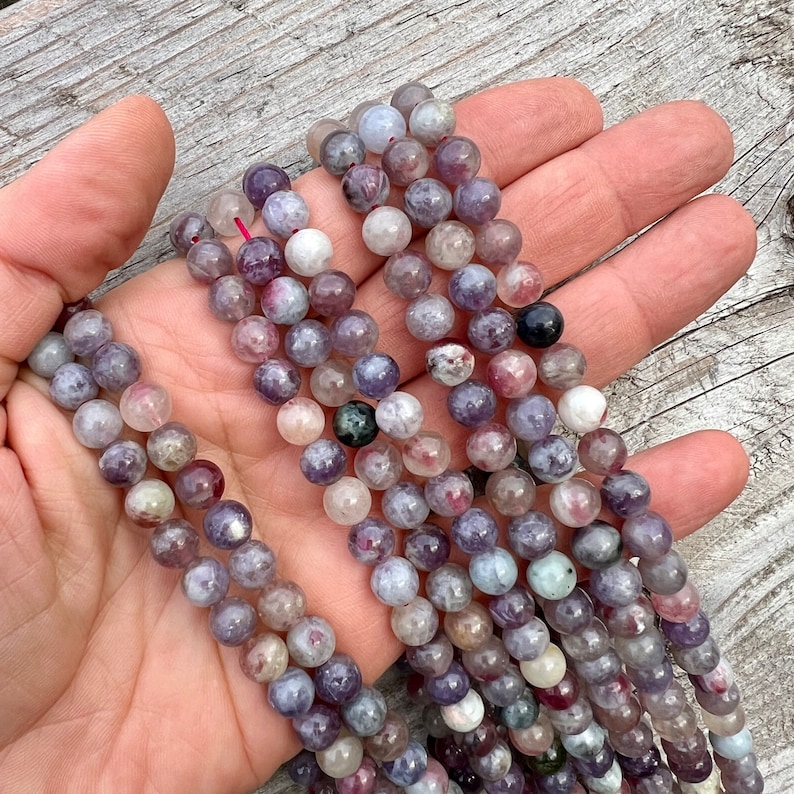 Cherry Tourmaline gemstone 8mm beads strands held in hand on a bright wood board in outdoors under natural daylight.
