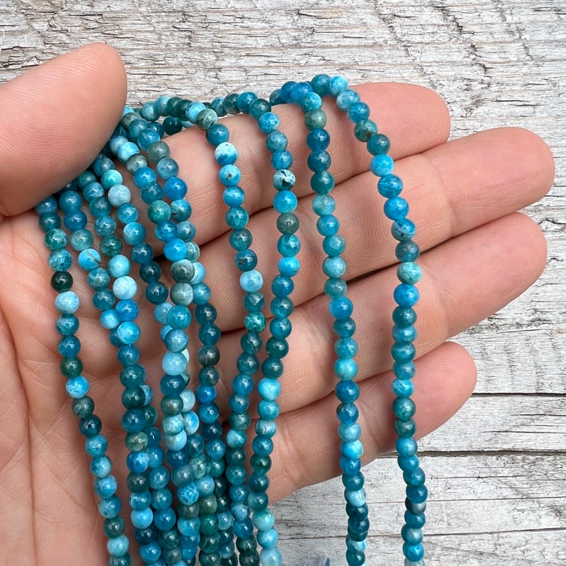 4mm Apatite stone beads strands held in hand on white background