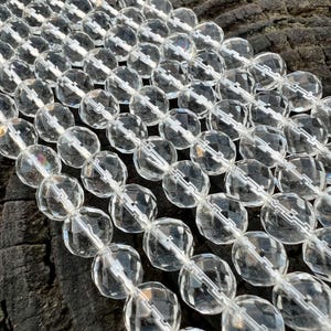 Könnte beinhalten: Eine Strähne aus klaren, facettierten Glasperlen. Die Perlen sind rund und haben eine leicht unregelmäßige Form. Sie sind auf einem klaren Faden aufgefädelt.
