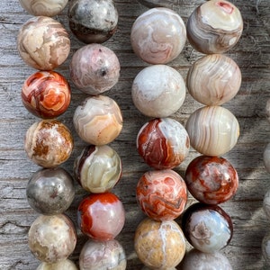 Laguna Lace Agate beads strands laid on a bright wood board in outdoors under natural daylight. these beads are white and gray and have lots of veins in various shapes and colors from red to brawn or pale blue. this picture is macro with details