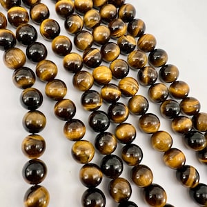 Può includere: Una collana di perle rotonde in occhio di tigre marrone e dorato. Le perle hanno una finitura naturale e lucida e sono infilate su un filo trasparente.