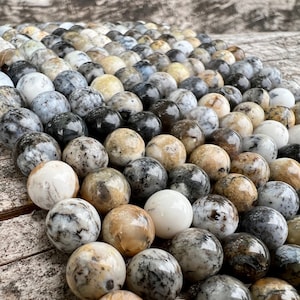 Könnte beinhalten: Nahaufnahme einer Schnur runder, polierter Achatperlen. Die Perlen sind eine Mischung aus Weiß, Grau und Braun mit komplizierten Mustern.