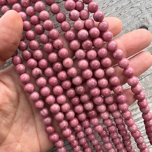 Rhodonite beads strands held in hand on a bright wooden board in outdoor under natural light. These are round 8mm beads with 1mm hole in middle for threading. they have a very delicate vein on them.