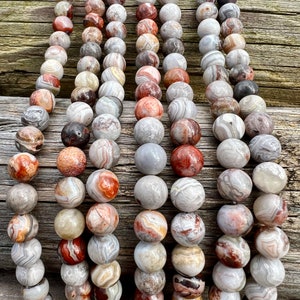 Laguna Lace Agate beads strands laid on a bright wood board in outdoors under natural daylight. these beads are white and gray and have lots of veins in various shapes and colors from red to brawn or pale blue