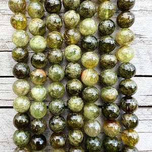 Pode incluir: Um fio de contas de pedras preciosas verdes e marrons. As contas são redondas e têm um acabamento liso e polido.