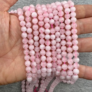 6mm Madagascar rose quartz beads strands held in hand on a grey background