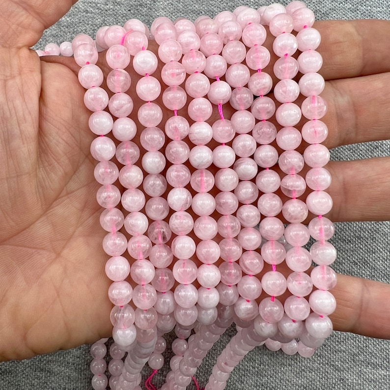 6mm Madagascar rose quartz beads strands held in hand on a grey background