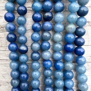 Może przedstawiać: Szereg niebieskich koralików z kamieni szlachetnych, w różnych odcieniach niebieskiego, ułożonych w rzędach. Koraliki są gładkie i okrągłe, z lekkim połyskiem.