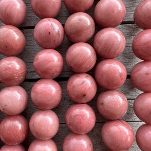 Rhodonite beads strands laid on a bright wooden board in outdoor under natural light. These are round 8mm beads with 1mm hole in middle for threading. they have a very delicate vein on them.