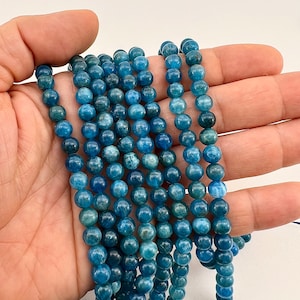 6mm Apatite stone beads strands held in hand on white background