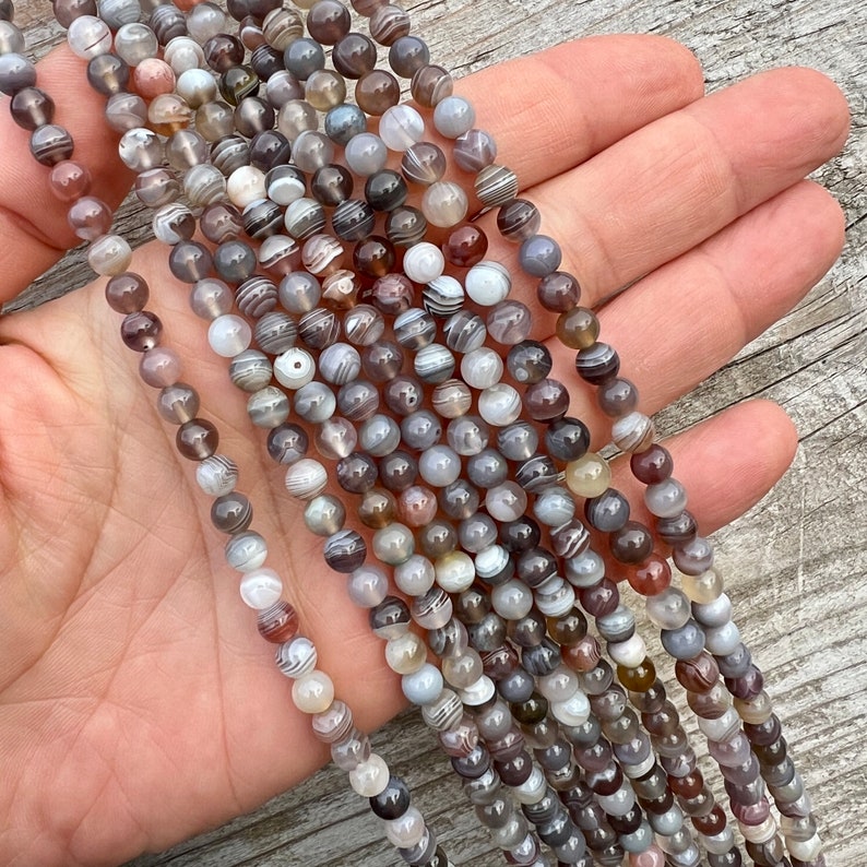 Botswana Agate 6mm beads strands held in hand on a bright wood board in outdoors under natural daylight.