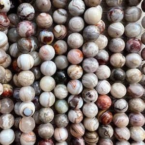 Laguna Lace Agate beads strands laid on a bright wood board in outdoors under natural daylight. these beads are white and gray and have lots of veins in various shapes and colors from red to brawn or pale blue