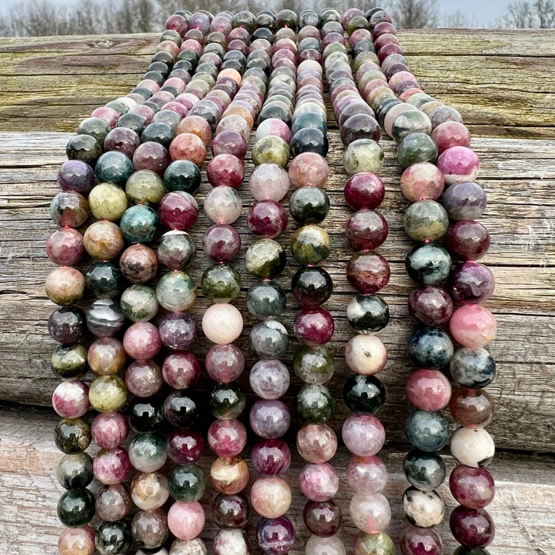 Tourmaline stone beads strands hanging over a bright wood board at outdoors and pictured under natural day light