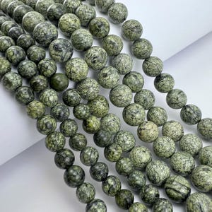 Peut inclure: Gros plan sur des perles rondes en serpentine verte. Les perles présentent un motif moucheté de vert foncé et de noir, créant un aspect texturé naturel. Idéal pour la création de bijoux.