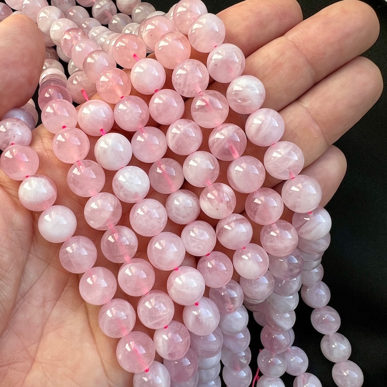 10mm Madagascar rose quartz beads strands held in hand on a black background