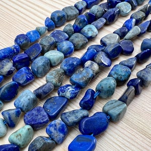 Könnte beinhalten: Eine Schnur polierter Lapislazuli-Edelsteinkugeln. Die Kugeln sind in einem Mix aus Dunkel- und Hellblau mit goldenen Pyrit-Flocken. Die Kugeln sind glatt und poliert.