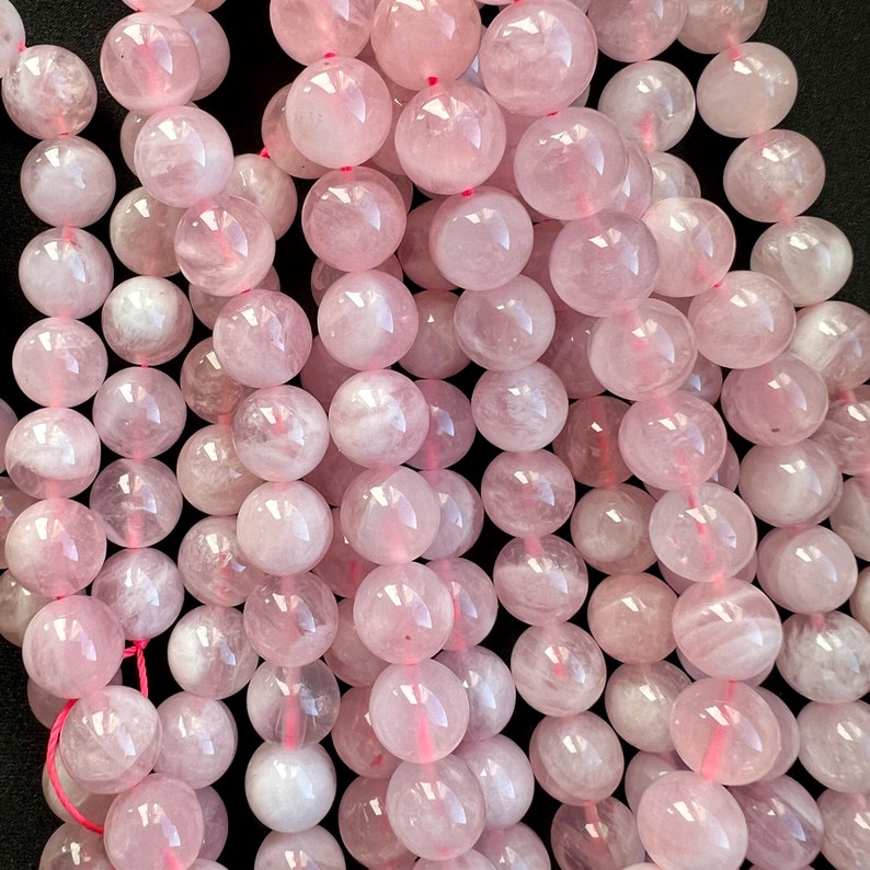 Madagascar rose quartz beads strands stacked laid on a black background. these beads have a pink color with withe hues.