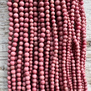 Rhodonite beads strands laid on a bright wooden board in outdoor under natural light. These are round 8mm beads with 1mm hole in middle for threading. they have a very delicate vein on them.