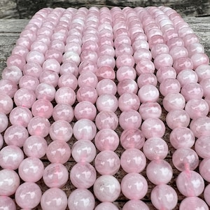 Peut inclure: Un brin de perles de quartz rose. Les perles sont lisses et polies, d'une couleur rose clair. Les perles sont disposées en rangées, créant un motif visuellement attrayant.