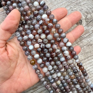 Botswana Agate 8mm beads strands held in hand on a bright wood board in outdoors under natural daylight.