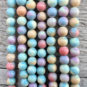 Könnte beinhalten: Eine Reihe runder, pastellfarbener Keramikperlen. Die Perlen sind eine Mischung aus hellblau, rosa und cremefarben mit Farbwirbeln in der gesamten Perle.