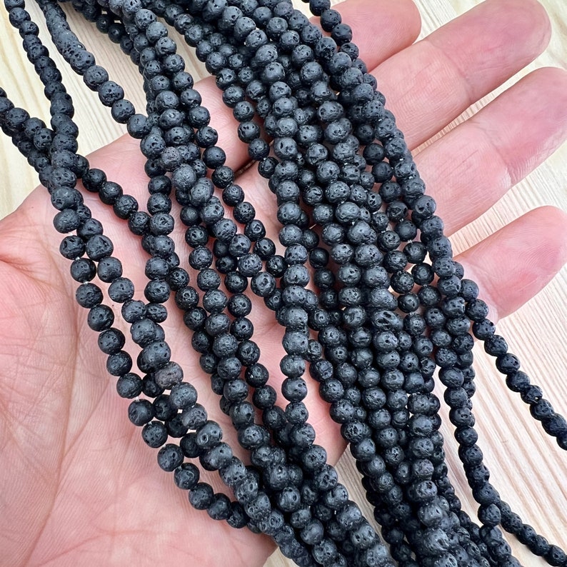 4mm lava beads strands held in hand on a bright wood board