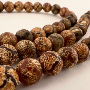May include: A strand of brown agate beads with a mottled pattern. The beads are round and have a smooth, polished finish.