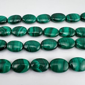 May include: Close-up of malachite beads. The oval-shaped beads are a deep green with distinctive swirling patterns. These polished beads are strung together, suitable for creating necklaces or other jewellery.