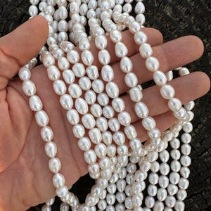 Puede incluir: Una hebra de perlas de agua dulce blancas, enhebradas en un hilo blanco. Las perlas son de forma ovalada y tienen un acabado liso y brillante.