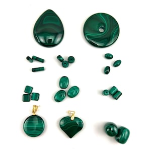 Op de afbeelding: Assortiment van gepolijste malachiet edelstenen en kralen in diverse vormen. Inclusief druppelvormige, ronde en hartvormige hangers met goudkleurige beugels, plus ovale, vierkante en cilindrische kralen. De malachiet is donkergroen met wervelende patronen.