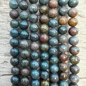 Può includere: Una collana di perle rotonde di pietre preziose verdi, marroni e rosa. Le perle sono lisce e lucidate.