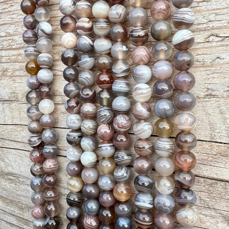 Botswana Agate beads strands lain on a bright wood board in outdoors under natural daylight.