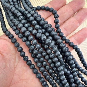 6mm lava beads strands held in hand on a bright wood board