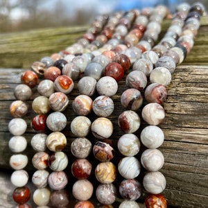 Laguna Lace Agate beads strands laid on a bright wood board in outdoors under natural daylight. these beads are white and gray and have lots of veins in various shapes and colors from red to brawn or pale blue