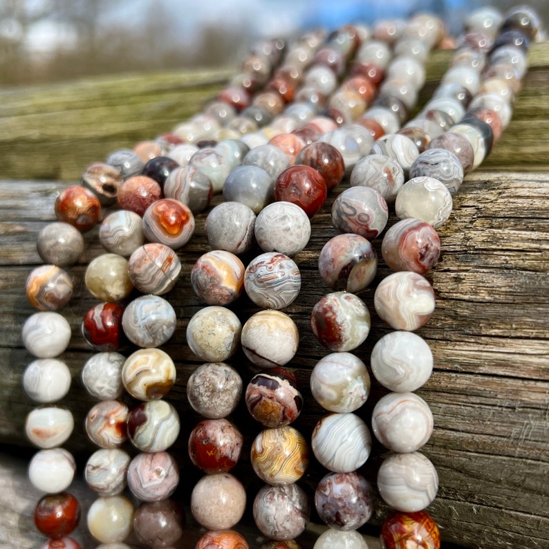 Laguna Lace Agate beads strands laid on a bright wood board in outdoors under natural daylight. these beads are white and gray and have lots of veins in various shapes and colors from red to brawn or pale blue