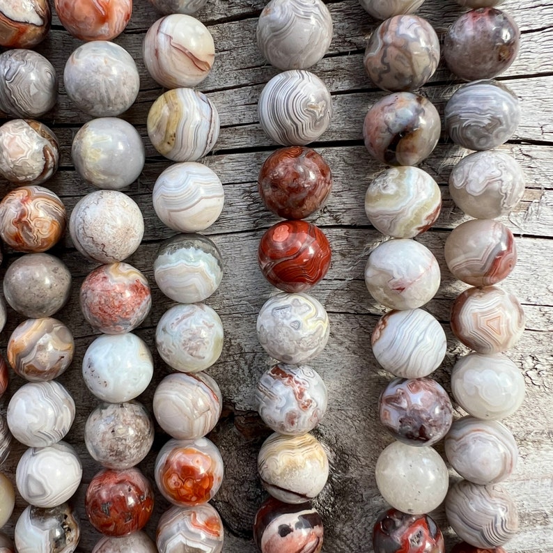 Laguna Lace Agate beads strands laid on a bright wood board in outdoors under natural daylight. these beads are white and gray and have lots of veins in various shapes and colors from red to brawn or pale blue