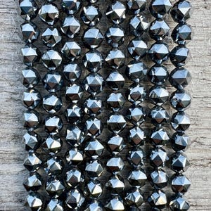 Könnte beinhalten: Eine Strähne schwarzer facettierter Edelsteinperlen. Die Perlen sind rund und haben eine glänzende, metallische Oberfläche.